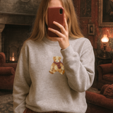 Person wearing a gray sweatshirt with a teddy bear design in a cozy room.
