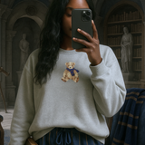 Person taking a selfie in a library wearing a sweater with a teddy bear design.