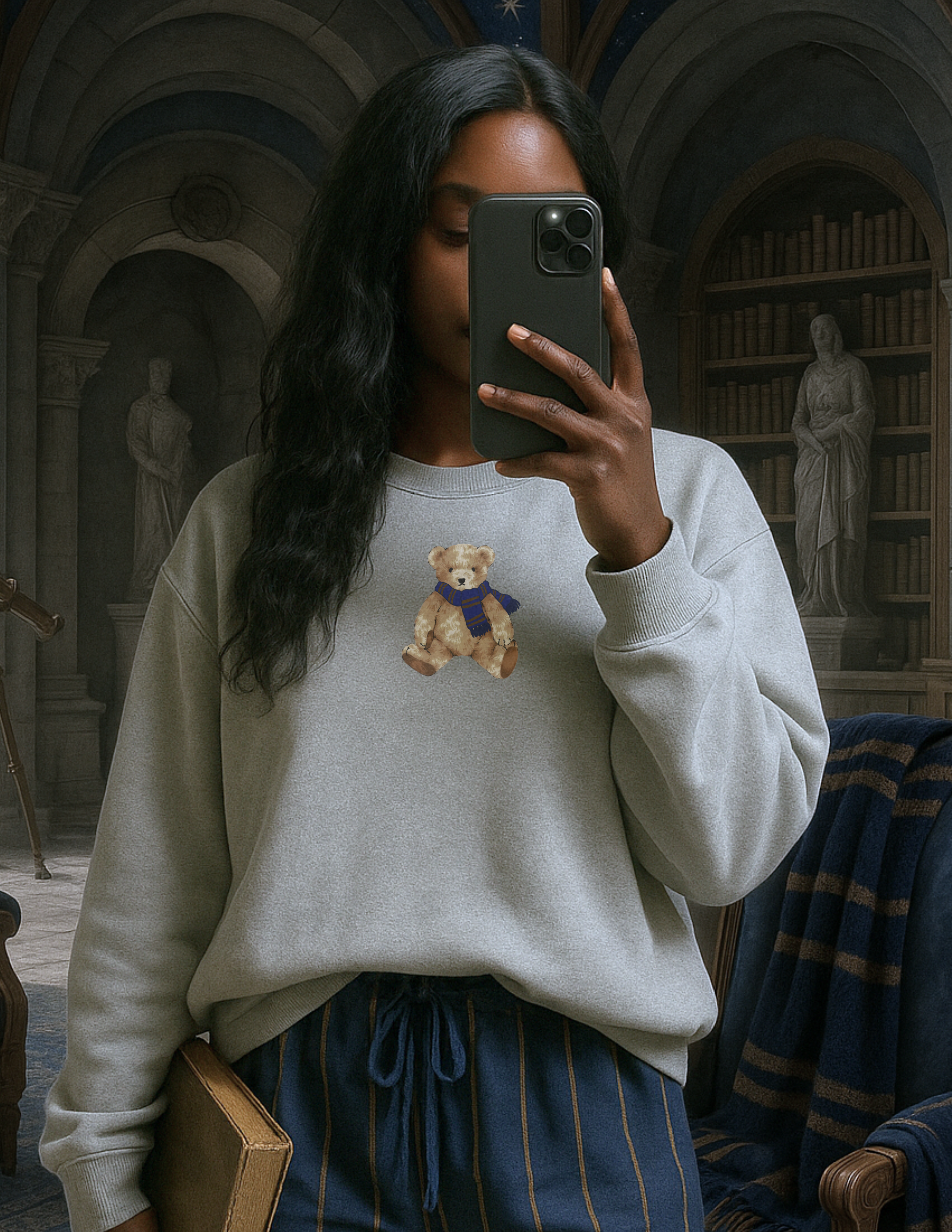 Person taking a selfie in a library wearing a sweater with a teddy bear design.