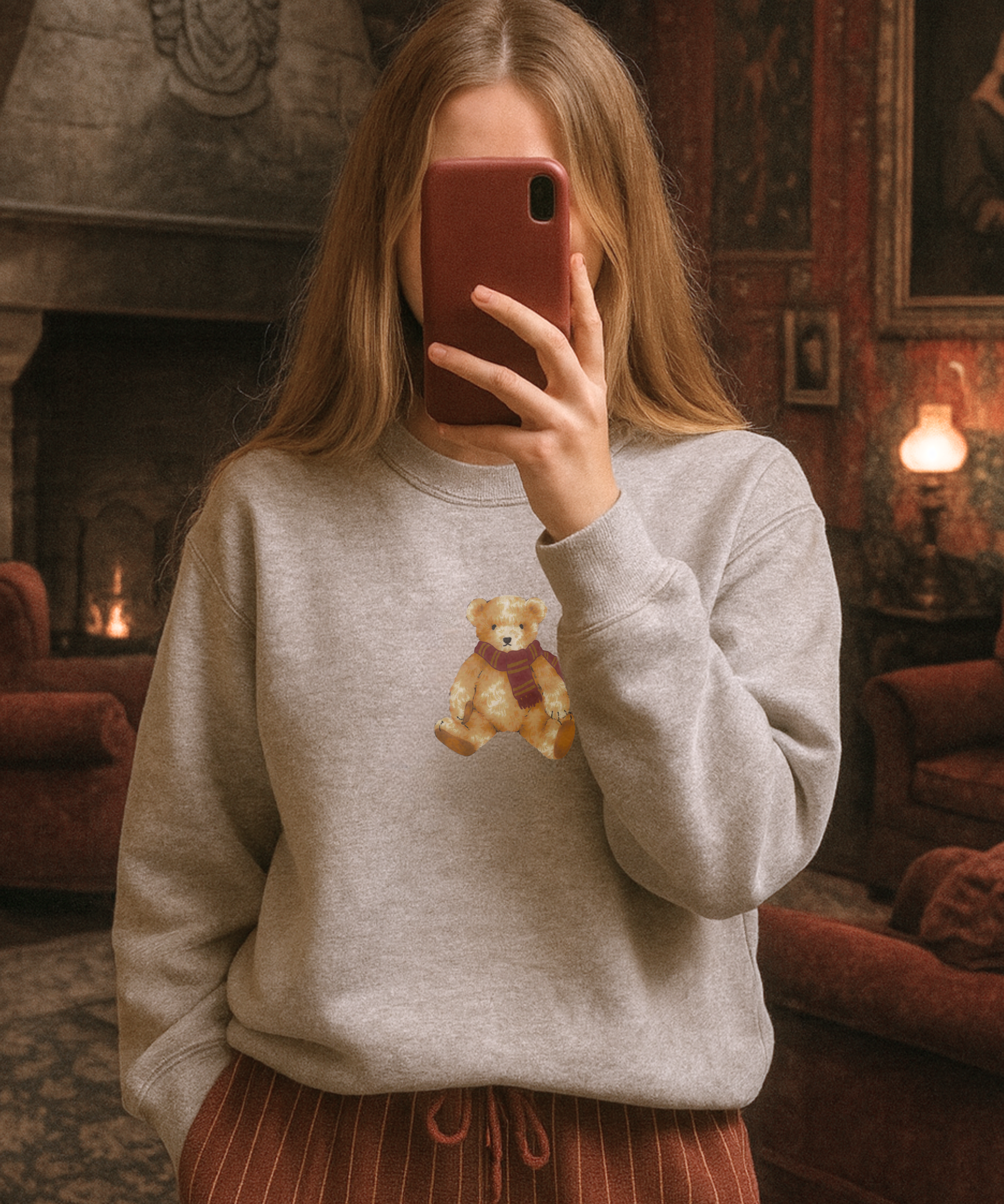Person wearing a gray sweatshirt with a teddy bear design in a cozy room.