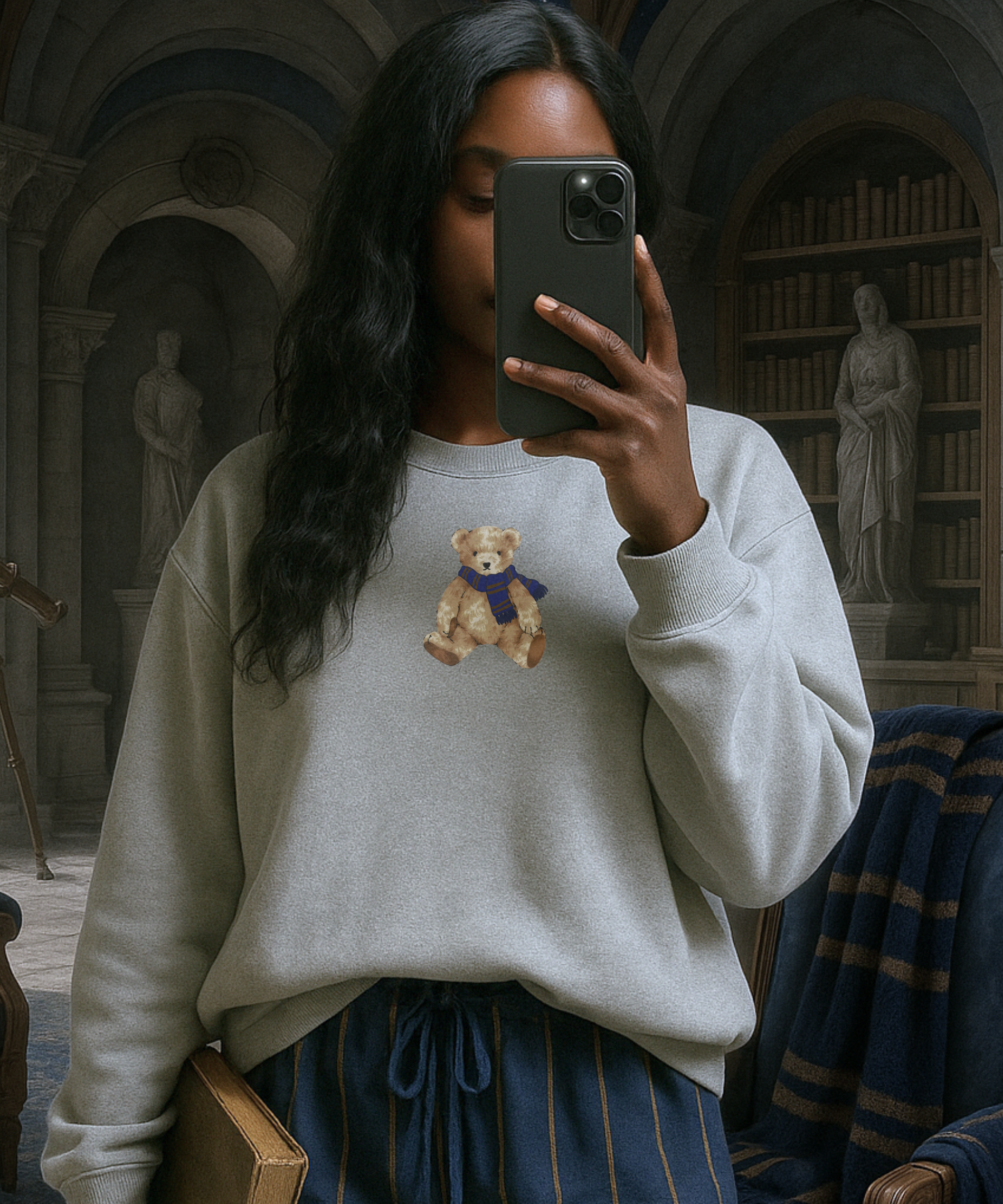Person taking a selfie in a library wearing a sweater with a teddy bear design.
